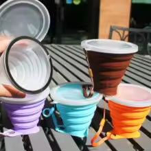 Colorful silicone foldable cup for kids with lids and carabiner clips displayed outdoors