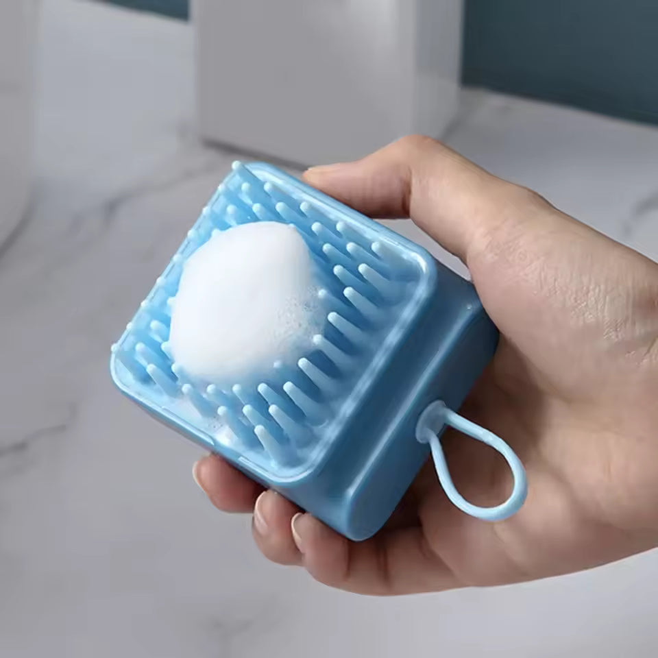 Hand holding blue silicone head massager brush with foam for scalp cleaning and massage