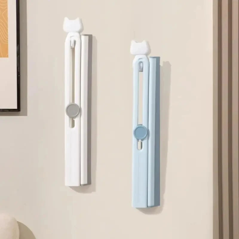 White and blue silicone shower squeegee with cat-shaped handles mounted on a beige wall
