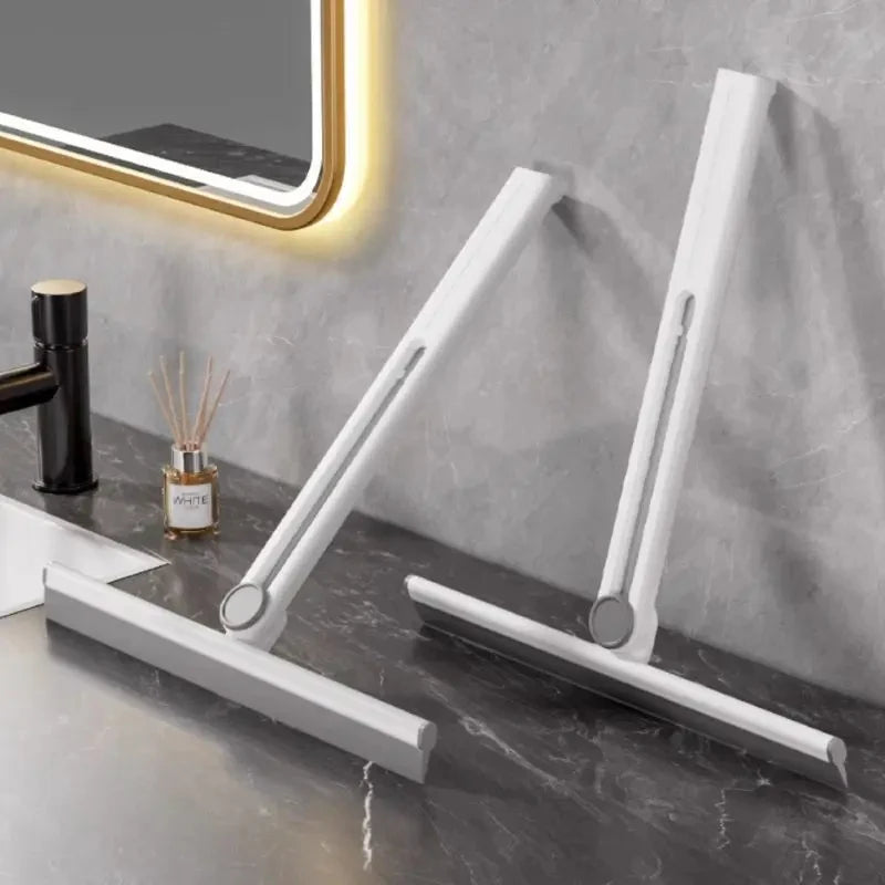 White silicone shower squeegee with foldable handle on bathroom countertop near black faucet and mirror