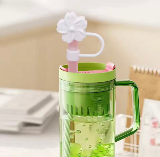 Green transparent cup with handle and pink silicone straw topped with a white flower silicone straw topper
