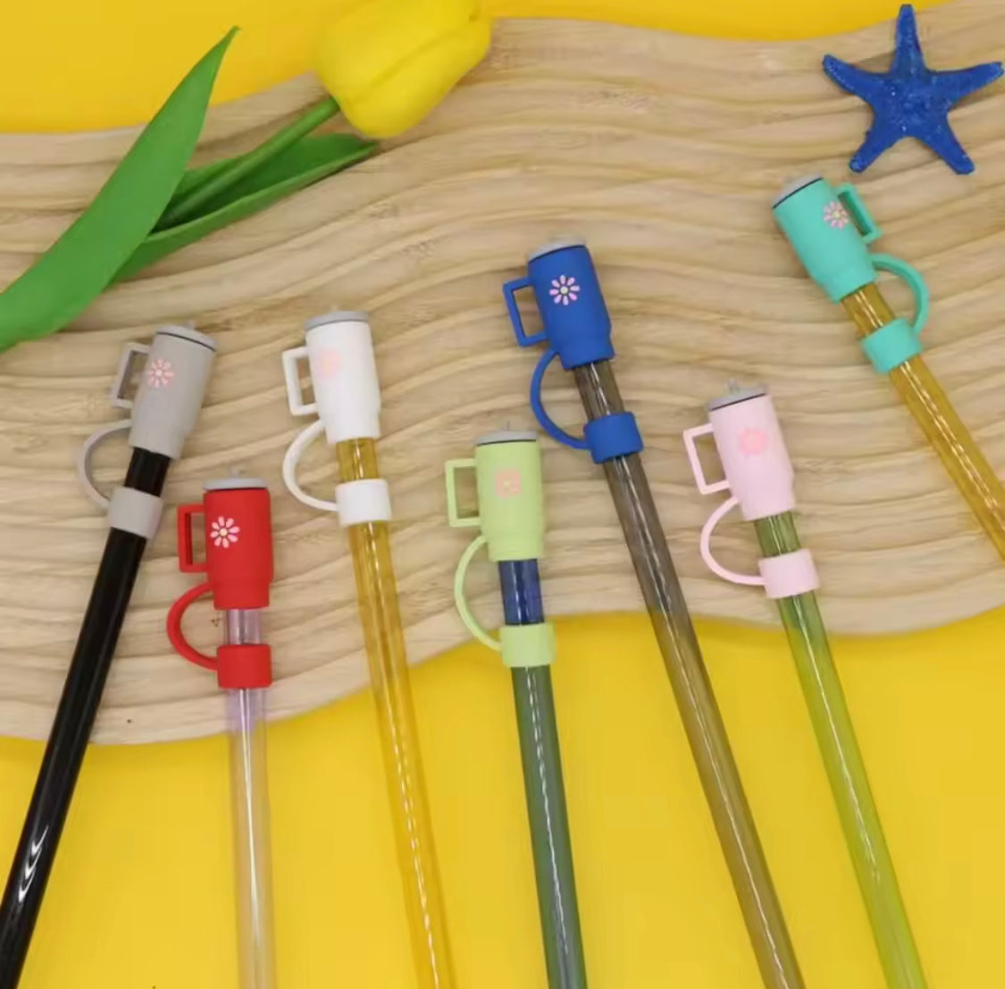 Colorful silicone straw toppers attached to reusable straws displayed on a wooden surface