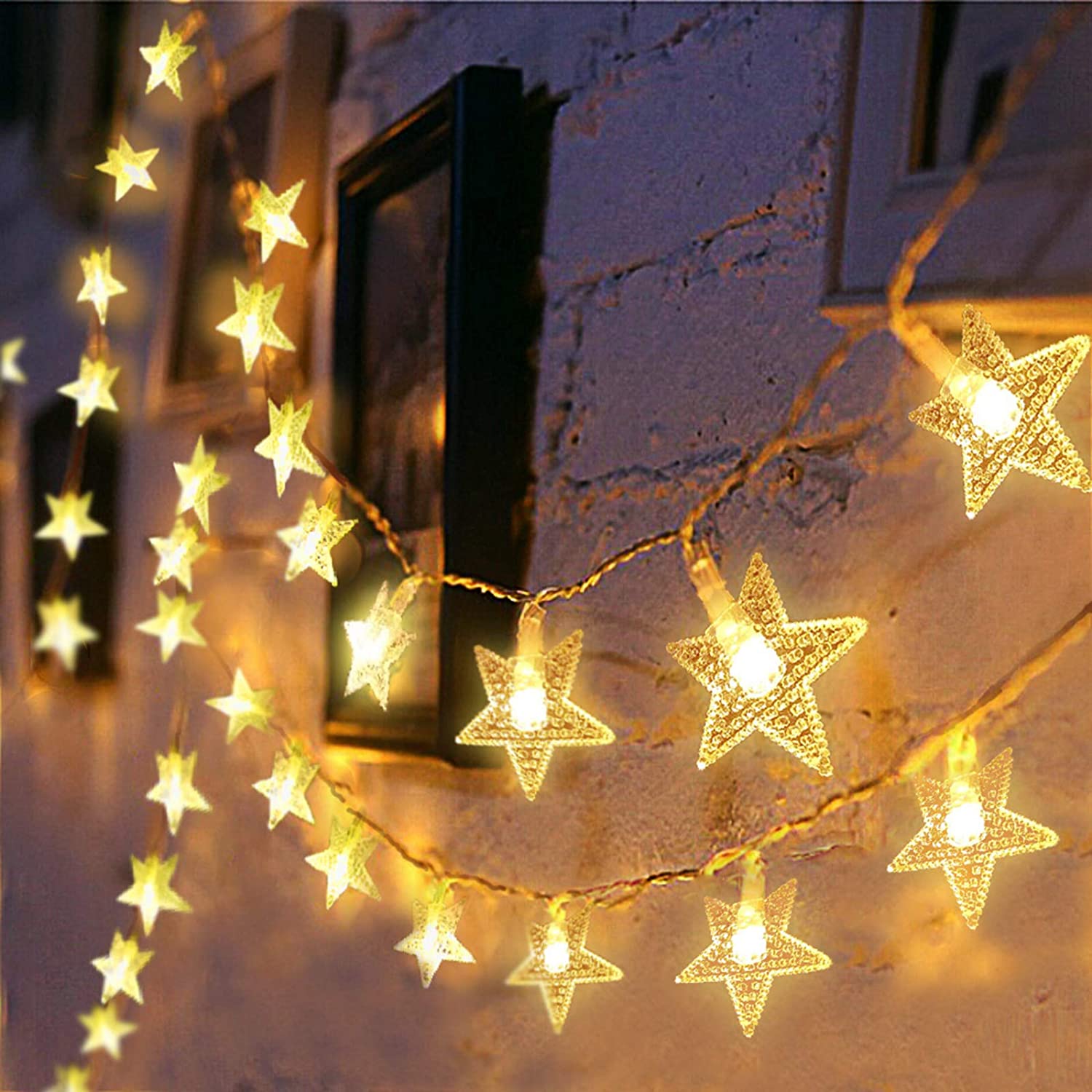 Warm glowing LED star curtain lights for decoration hanging on a textured wall with framed pictures
