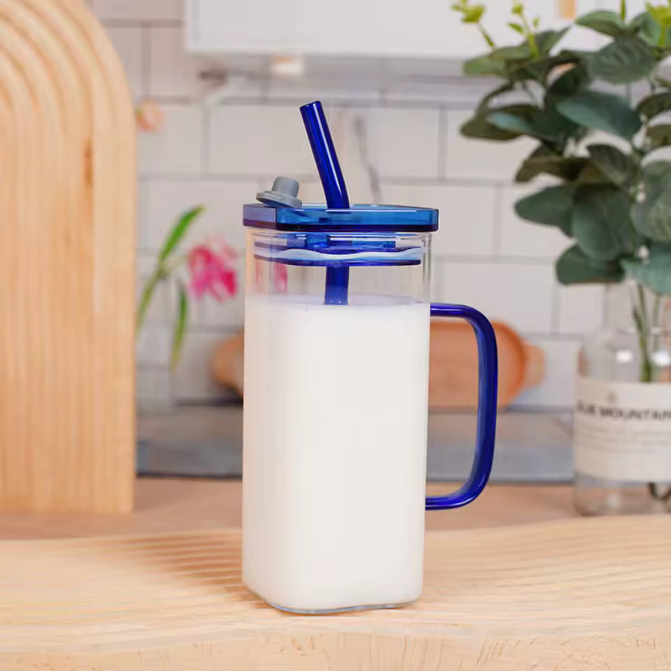 Clarify.pk transparent glass bottle coffee mug with blue lid and straw filled with milk on wooden table