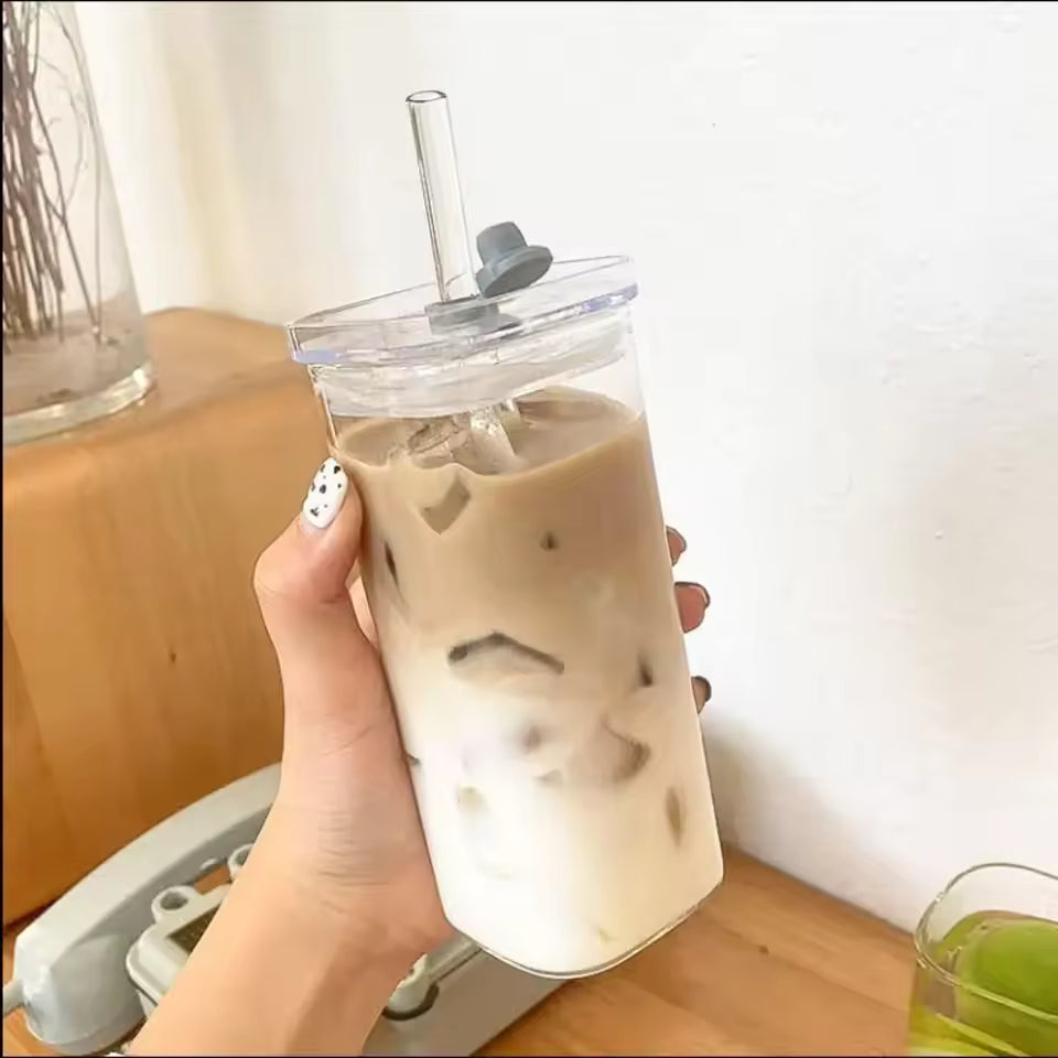 Hand holding Clarify.pk transparent glass bottle filled with iced coffee and a clear straw