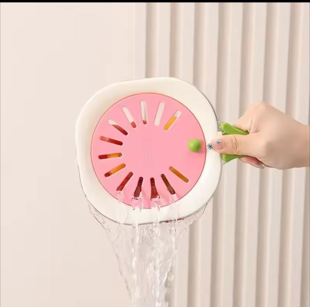 Hand holding a pink and white kitchen strainer with water pouring through in a modern kitchen