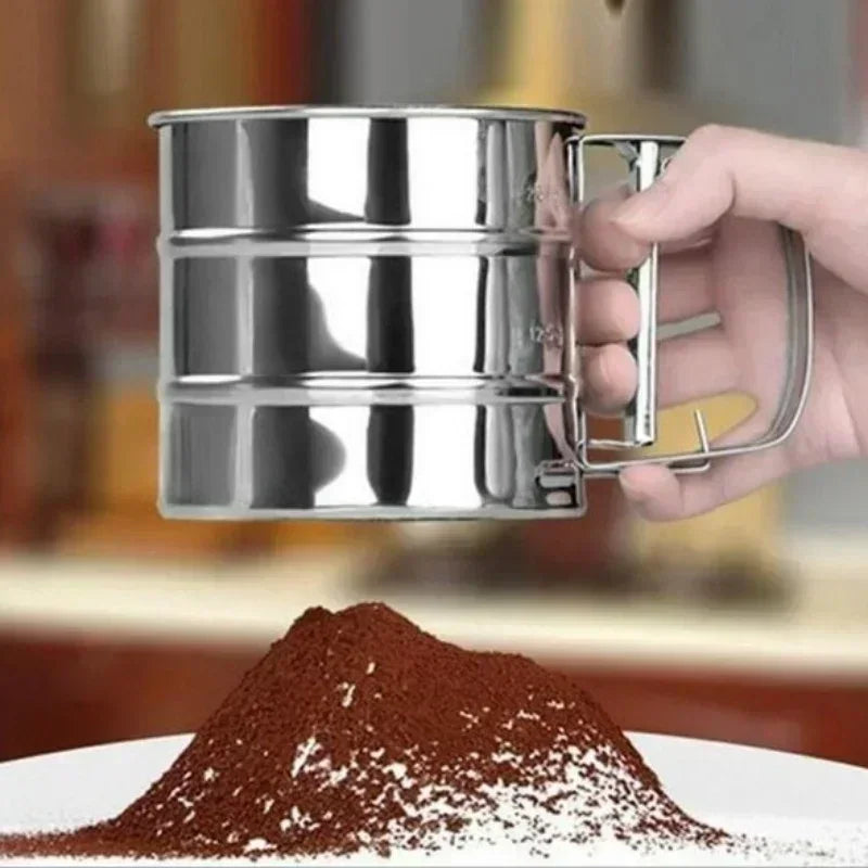 Hand holding a stainless steel flour sieve above a plate of sifted cocoa powder