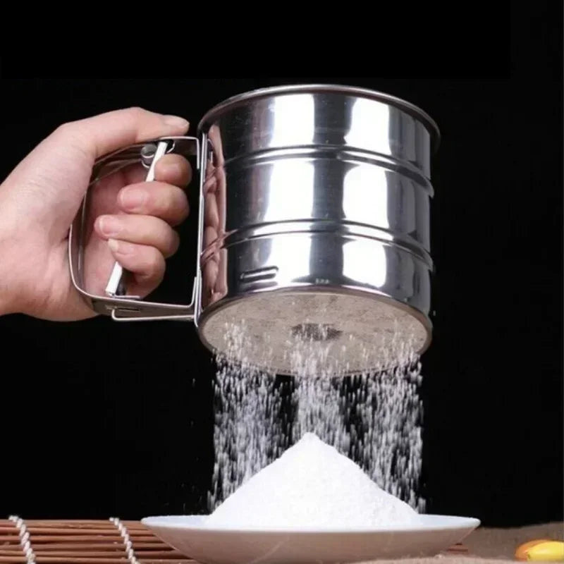 Hand holding a stainless steel flour sieve sifting flour onto a white plate with a black background
