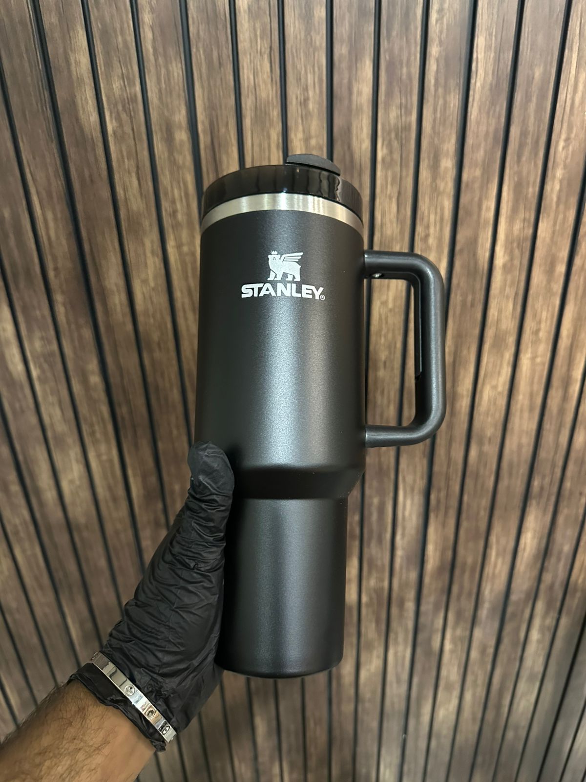 40oz stainless steel tumbler with handle in black held against wooden background