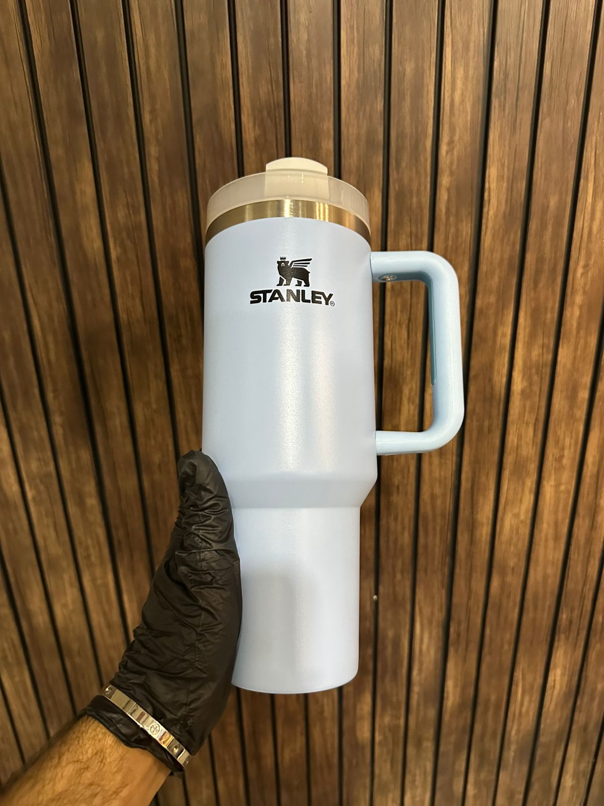 40oz stainless steel tumbler with handle in white held against wooden background by hand wearing black glove