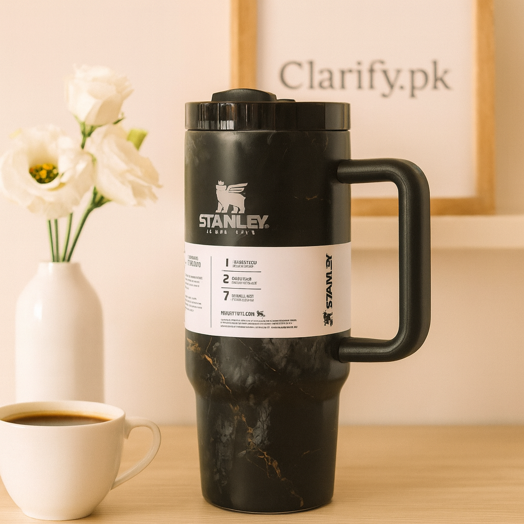 Stanley black tumbler with handle and marble finish on wooden table beside white coffee cup and flowers