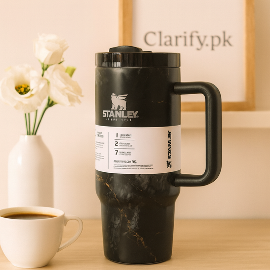 Stanley black tumbler with handle and marble finish on wooden table beside white coffee cup and flowers