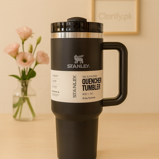 Black Stanley quencher tumbler with handle and lid placed on wooden surface with flowers in the background