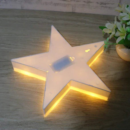 Clarify.pk star shape LED night lamp glowing with warm light on wooden surface next to green plant