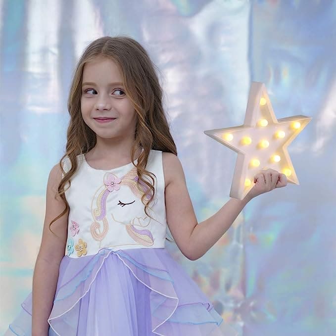 Young girl holding a star shape LED night lamp glowing with warm lights in a pastel dress