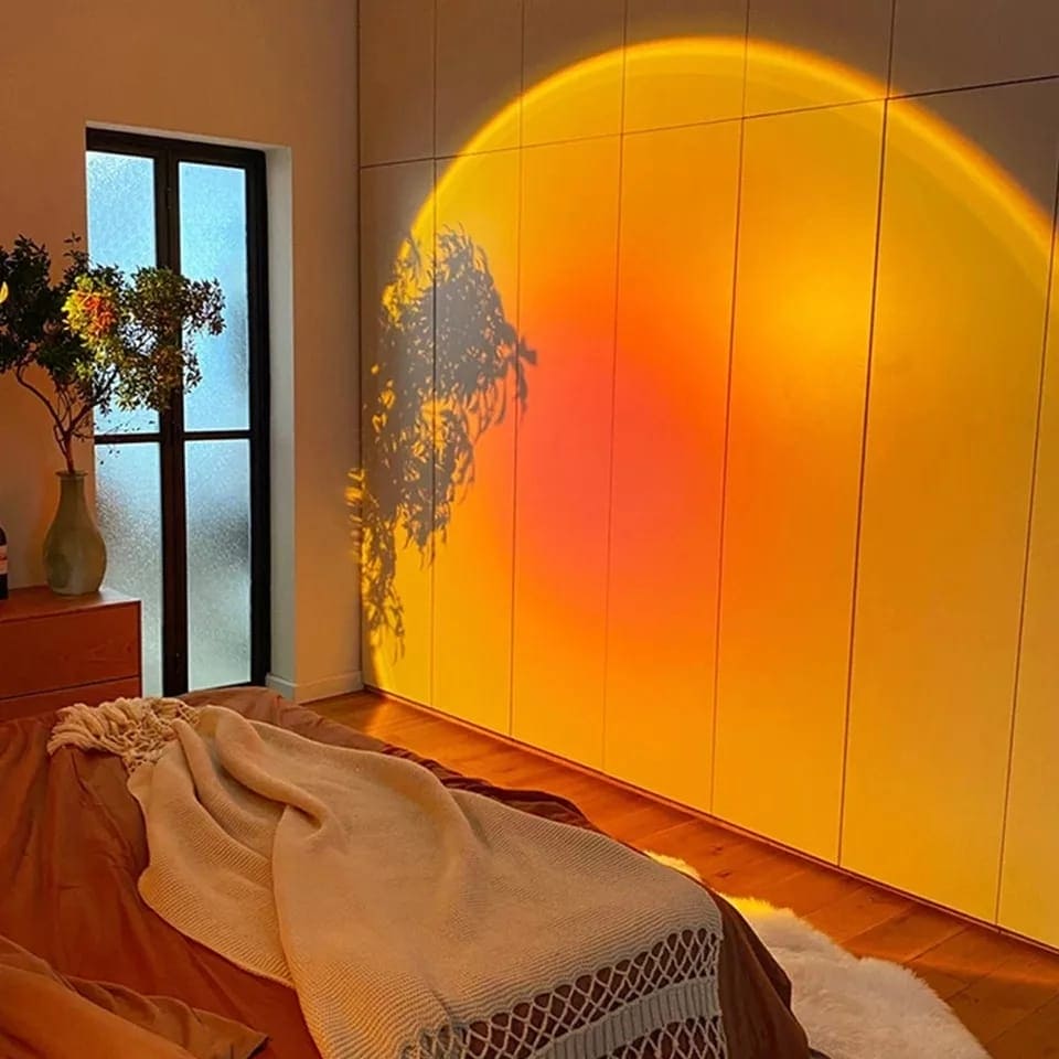 Warm sunset projector lamp for bedroom casting orange and yellow light on bedroom wall with cozy bed and blanket