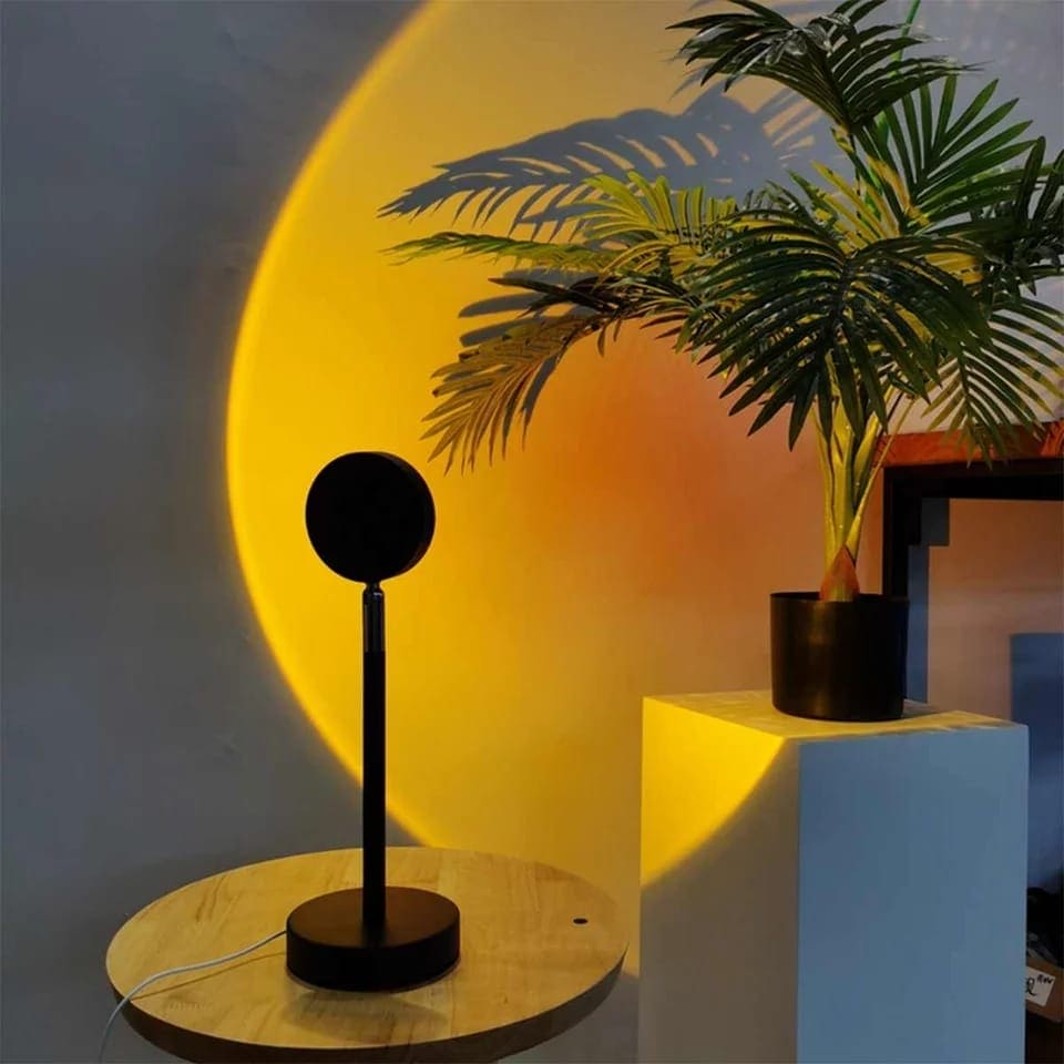 Modern black sunset projector lamp for bedroom casting warm yellow and orange light with plant shadows