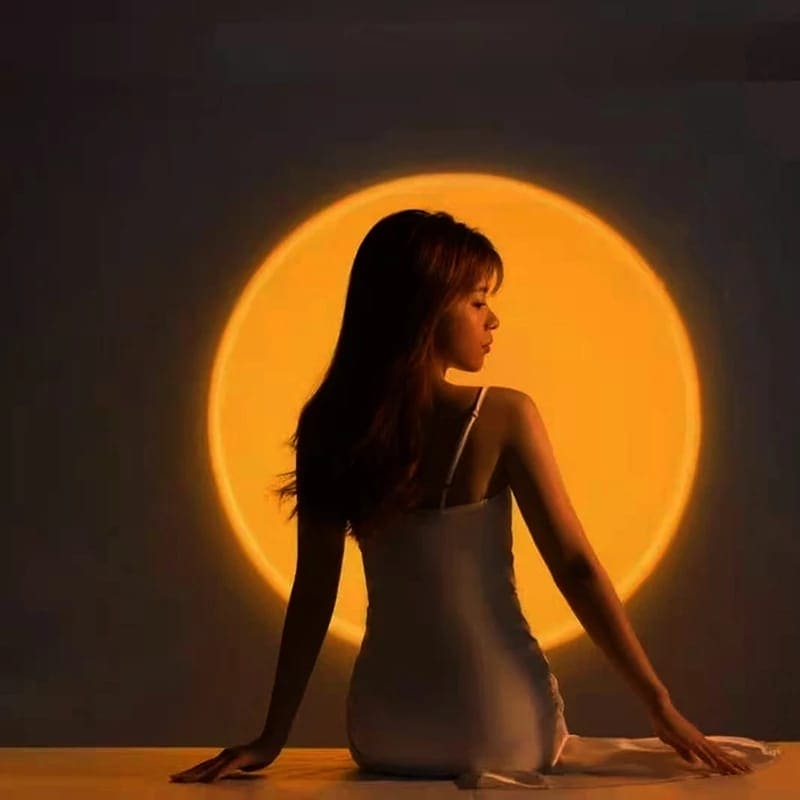 Woman sitting in front of a glowing yellow orb created by a sunset projector lamp for bedroom ambiance