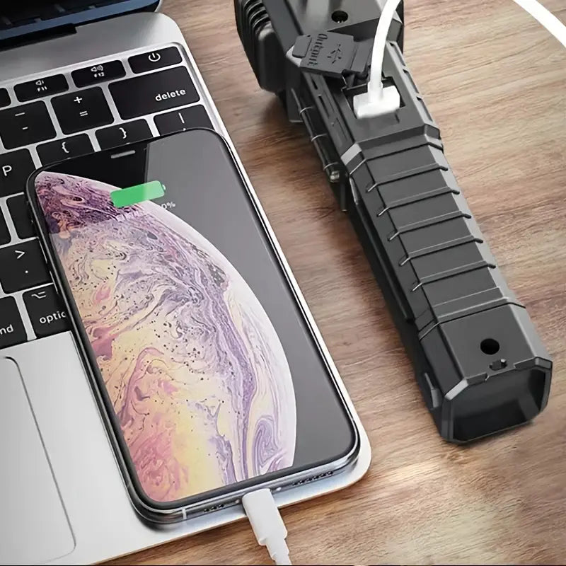 Super bright led flashlight charging next to a smartphone on a laptop keyboard
