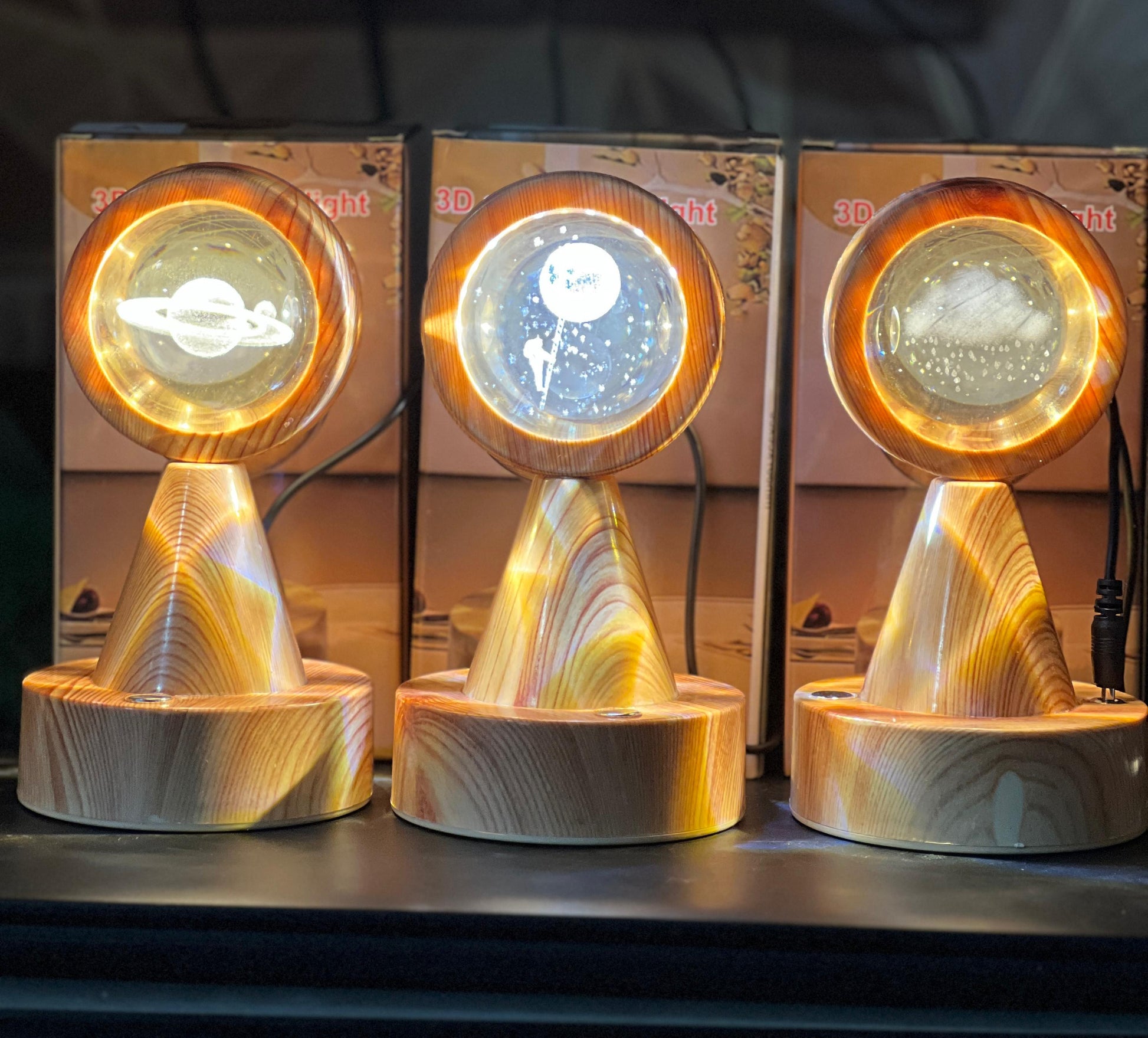 Three wooden crystal globe projector lamps displaying different planetary designs with glowing rings