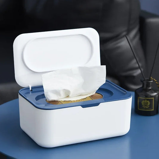 White tissue storage box with lid open showing tissue paper on blue surface next to diffuser bottle