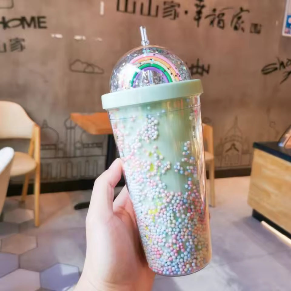 Hand holding a unicorn water cup with straw filled with colorful foam beads and a rainbow decoration