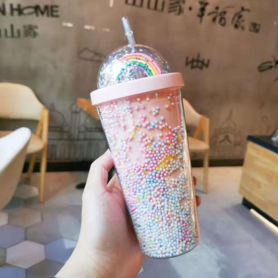 Hand holding unicorn water cup with straw filled with colorful beads and rainbow design lid