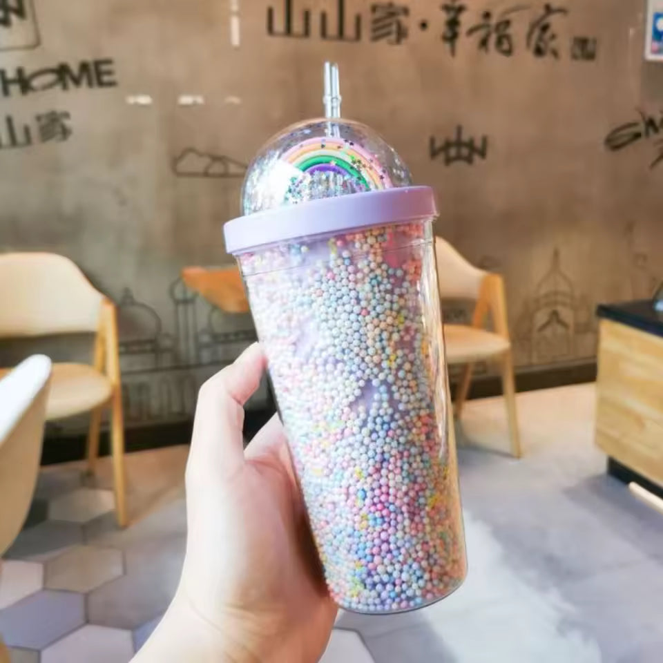 Hand holding unicorn water cup with straw filled with colorful foam beads in a cafe setting