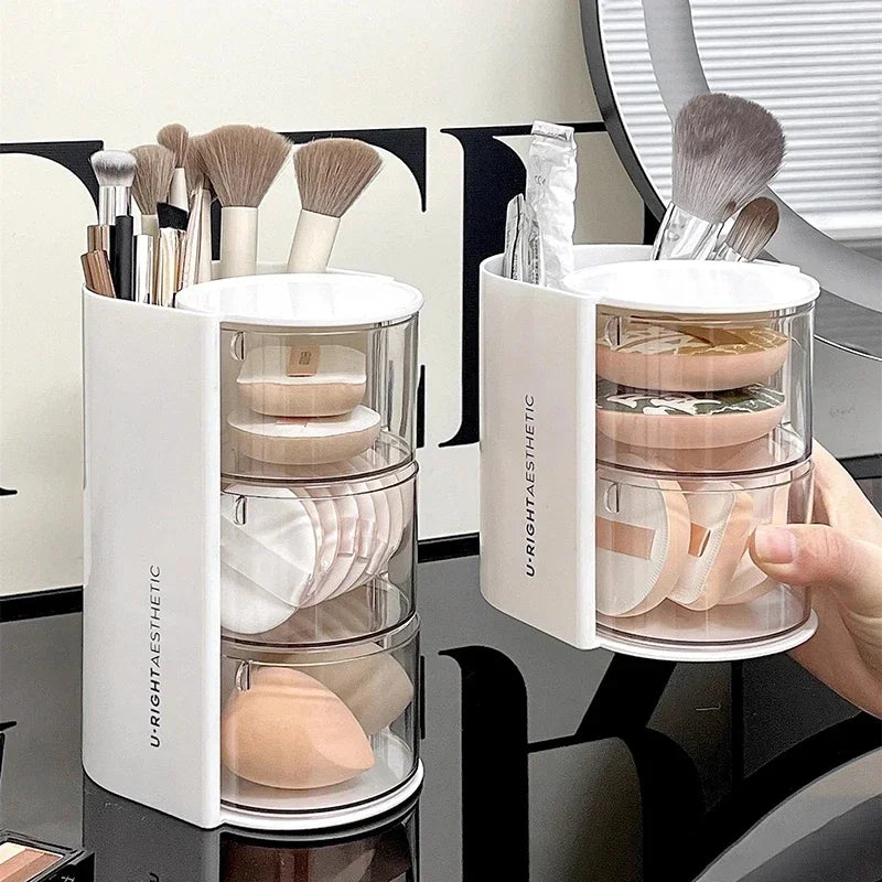 White 3 layer cosmetic storage box holding makeup brushes, sponges, and beauty tools on a black surface