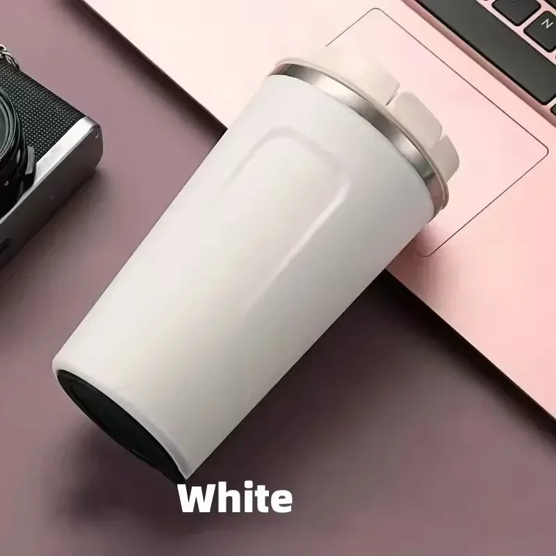 White vacuum thermos bottle for tea and coffee placed beside a laptop and camera on a desk