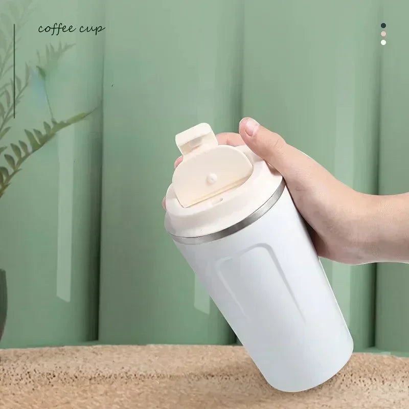 Hand holding white vacuum thermos bottle for tea and coffee with flip lid on beige surface