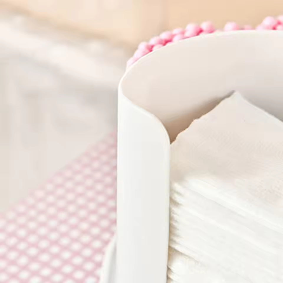 White 2 in 1 qtip holder and tissue dispenser with stacked napkins on a pink patterned surface