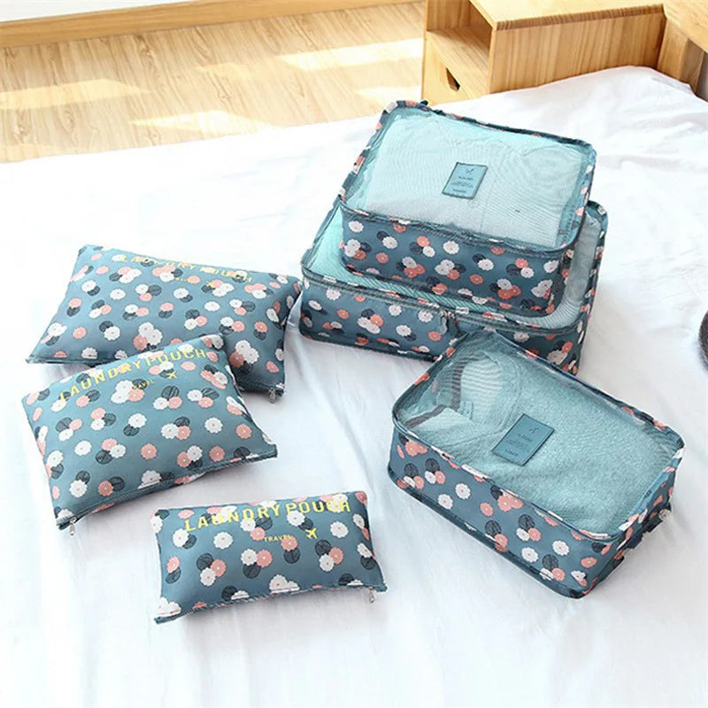 Blue floral 6 piece luggage organizer set with mesh top compartments and laundry pouches on white bed