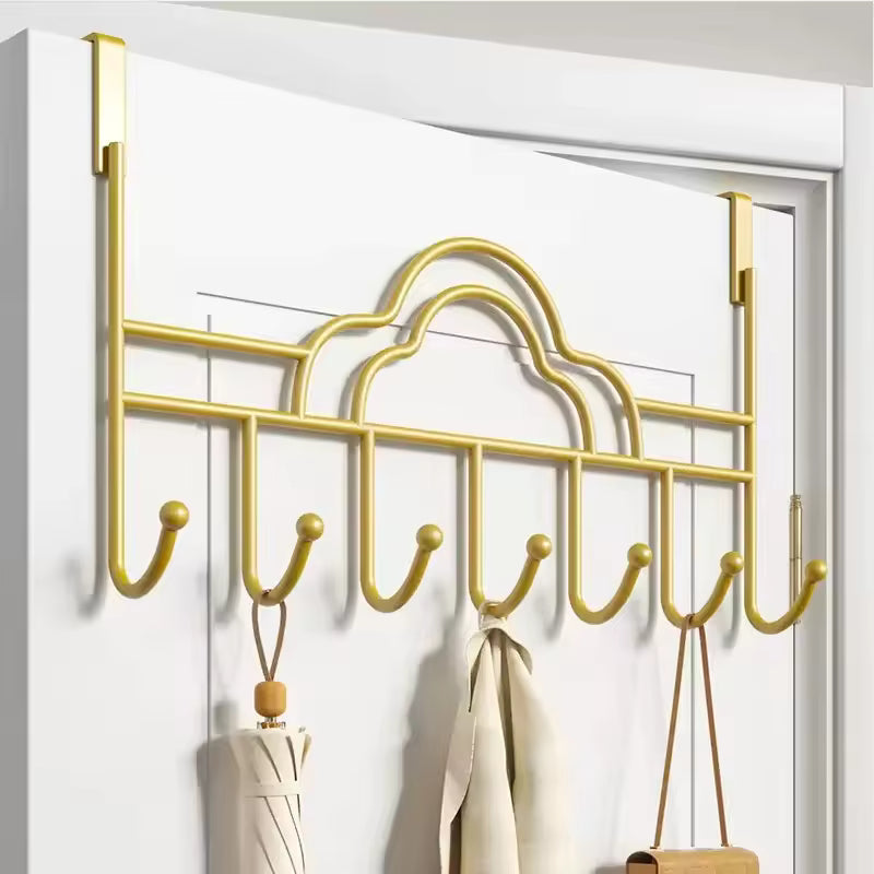 Gold metal behind door hooks for clothes with seven curved hooks hanging on a white door