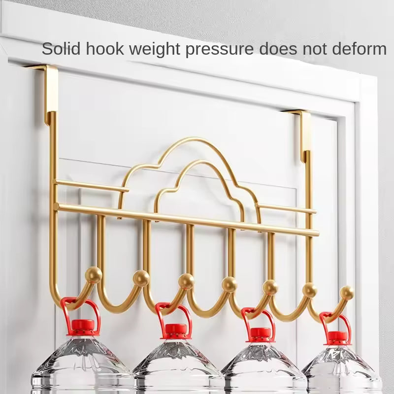 Gold metal behind door hooks for clothes holding multiple large water bottles on white door