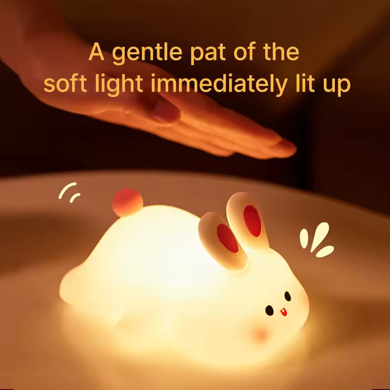 Cute rabbit desk lamp glowing with soft light under a hand in a dark room