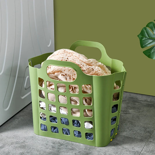 Green foldable plastic laundry basket filled with clothes placed on a gray floor