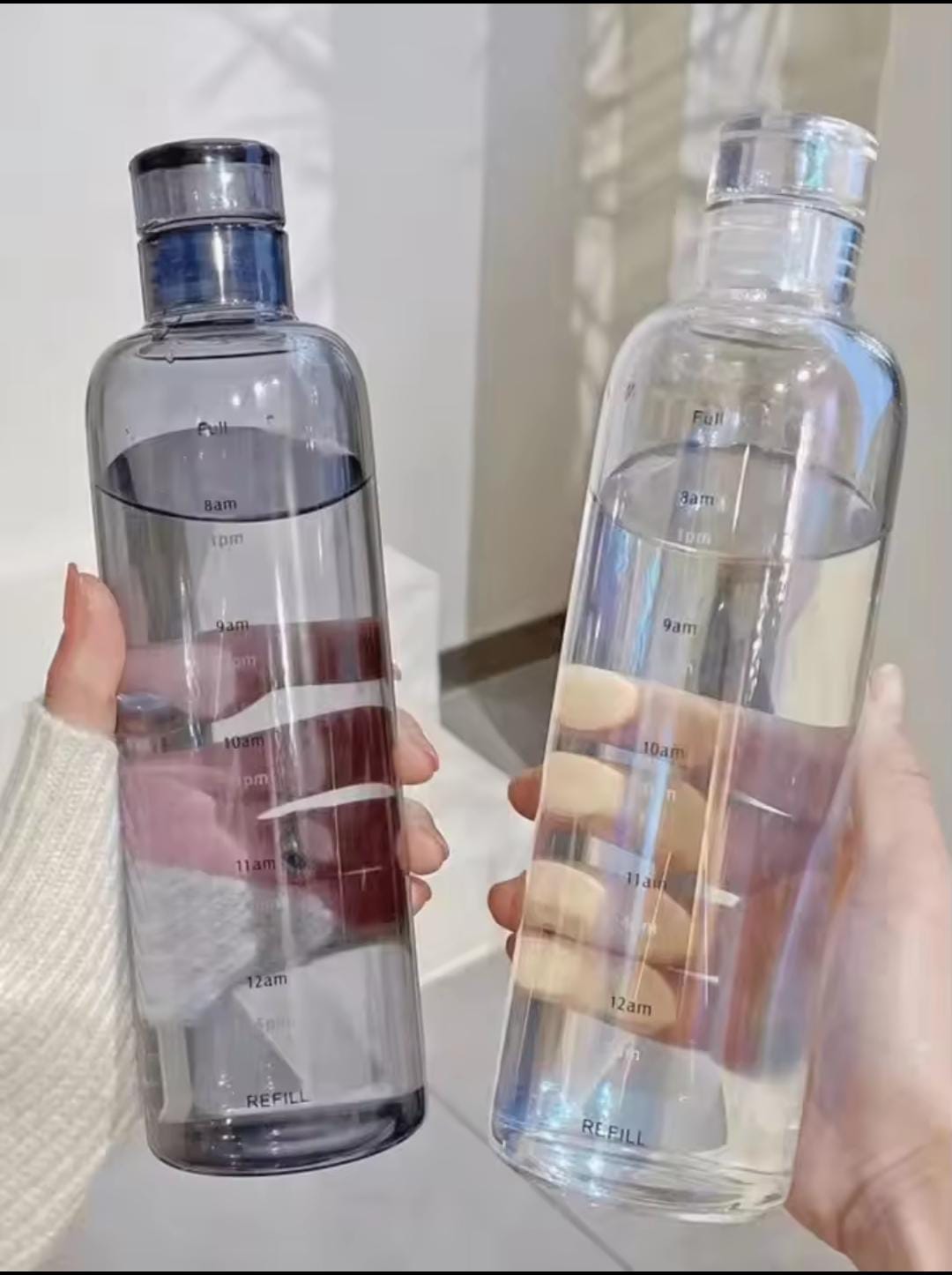 Two hands holding transparent plastic water bottle 500ml with time markings for daily hydration tracking