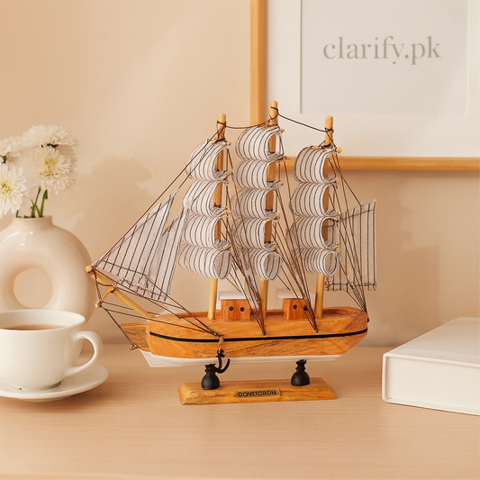Vintage wooden ship showpiece with white sails displayed on a wooden table next to a cup and book