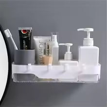Clear wall-mounted bathroom shelf holding toiletries including pump bottles and tubes near mirror