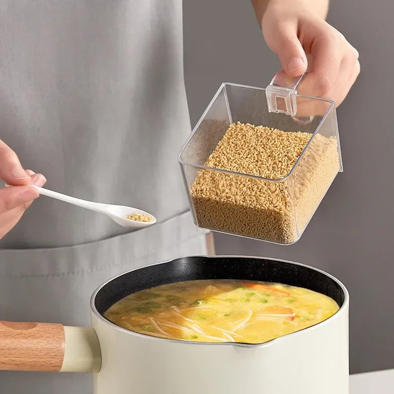 Hand holding clear container from wall mounted spice box scooping spice into pot of soup