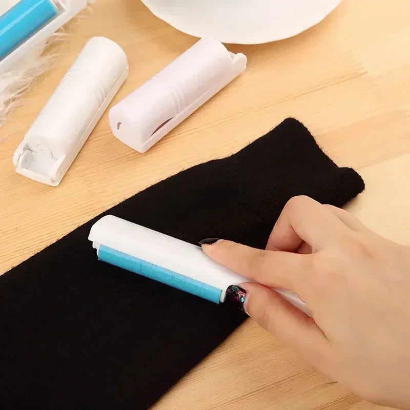 Hand using washable lint remover brush on black fabric with two white brush refills on wooden surface