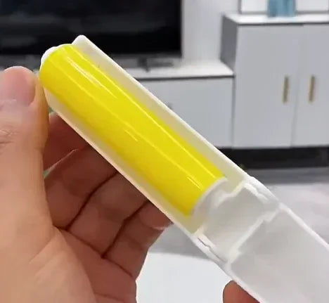 Hand holding a washable lint remover brush with a yellow roller in a white plastic casing