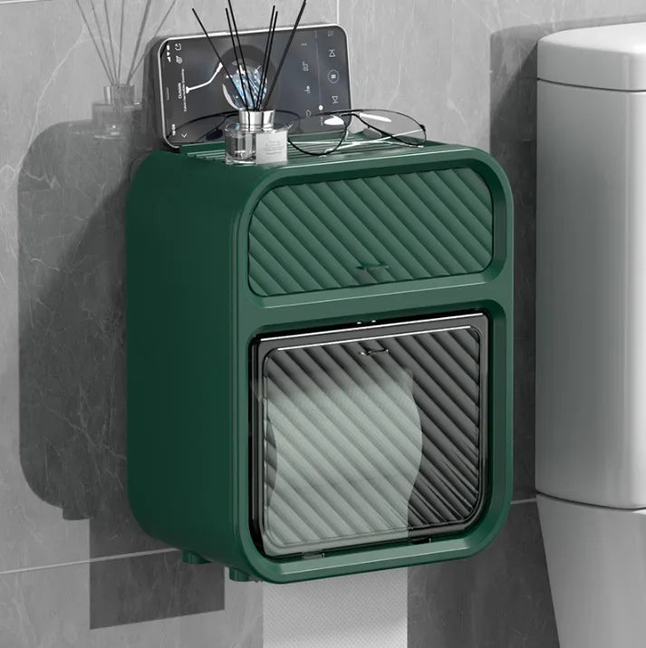 Green waterproof bathroom tissue box mounted on wall next to toilet with phone and glasses on top