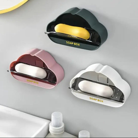 Three whimsical cloud soap dish holders in green, pink, and white colors mounted on a bathroom wall