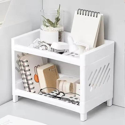 White double layer desk organizer holding notebooks, glasses, charger cables, and small plant on a white desk