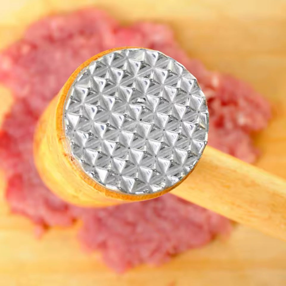 Close-up of wooden meat tenderizer hammer with metal textured head resting on raw meat