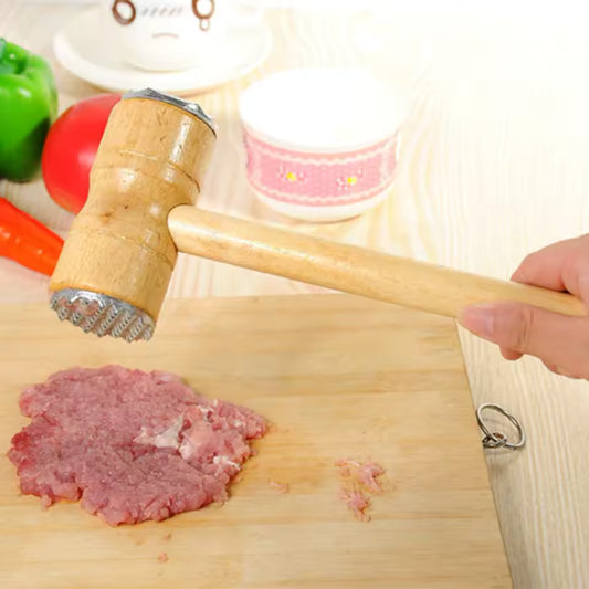 Person using wooden meat tenderizer hammer to flatten raw meat on wooden cutting board