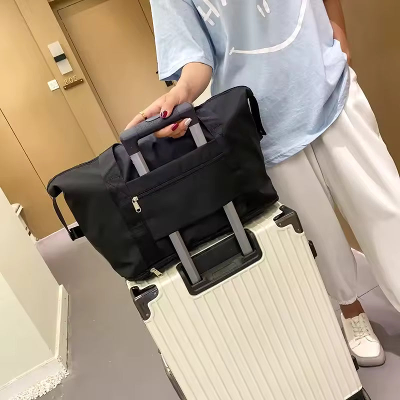 Black large capacity travel bag placed on a white hard-shell suitcase with retractable handle