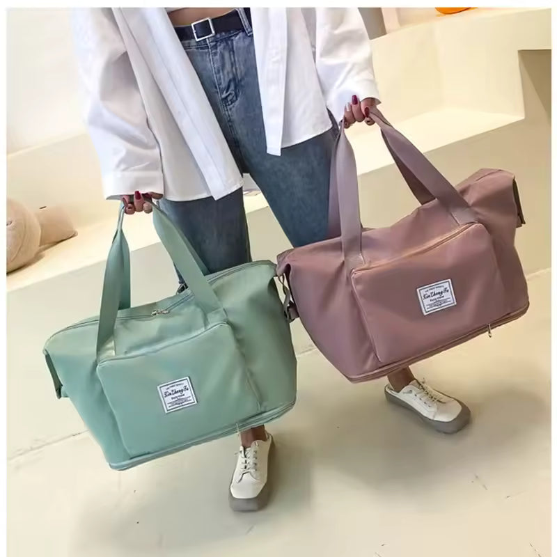 Person holding two large capacity travel bags in green and pink with front pockets and dual handles